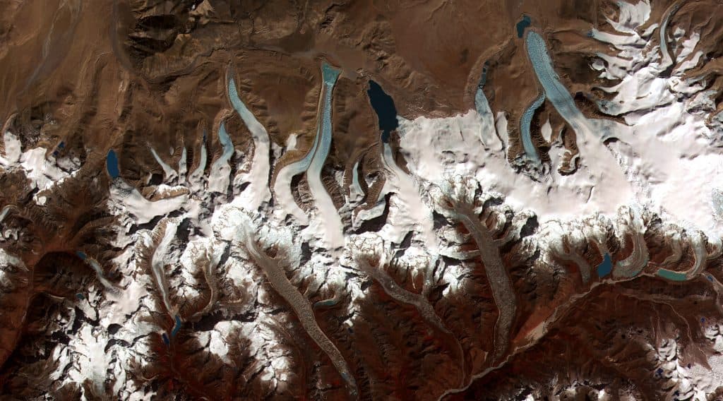 Bird's eye vie of a mountainous glacier, white on deep brown, fingers of glacial lakes a light aquamarine