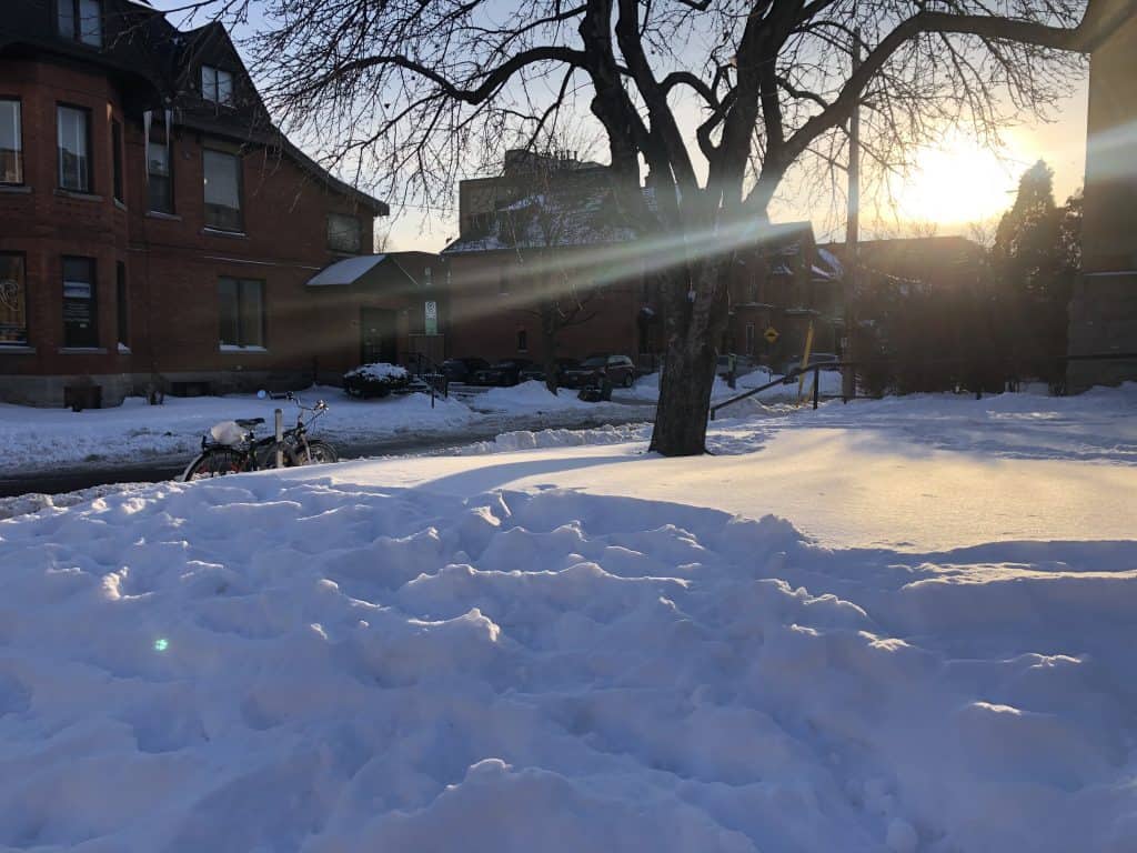 winter photo of sun hanging low over a city with snow in the foreground