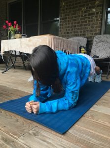 A person with long hair is planking on a yoga mat.